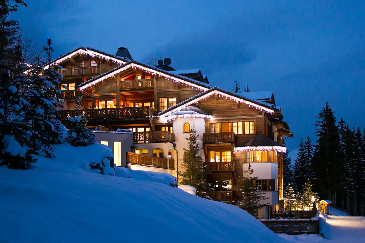 A view of ski chalets at nighttime, warm lights glowing from inside