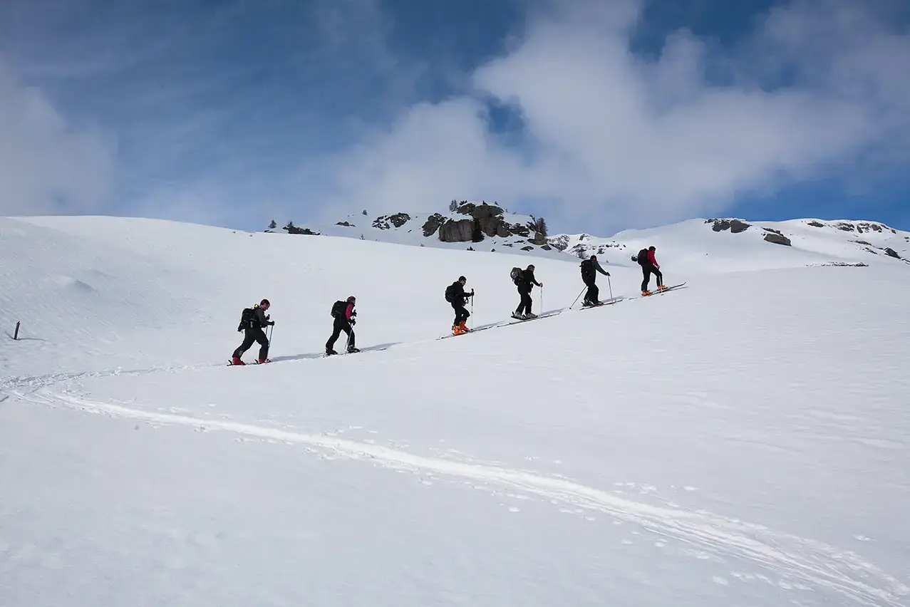 Six skiers hiking across a snowy expanse all in a line