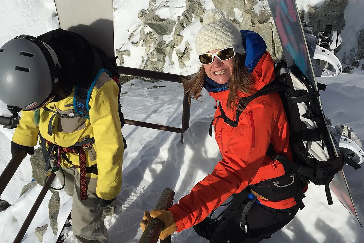 Swisskisafari founder, Danieelle Stynes, smiling at the camera crouched down in the snow during a snowboarding excursion