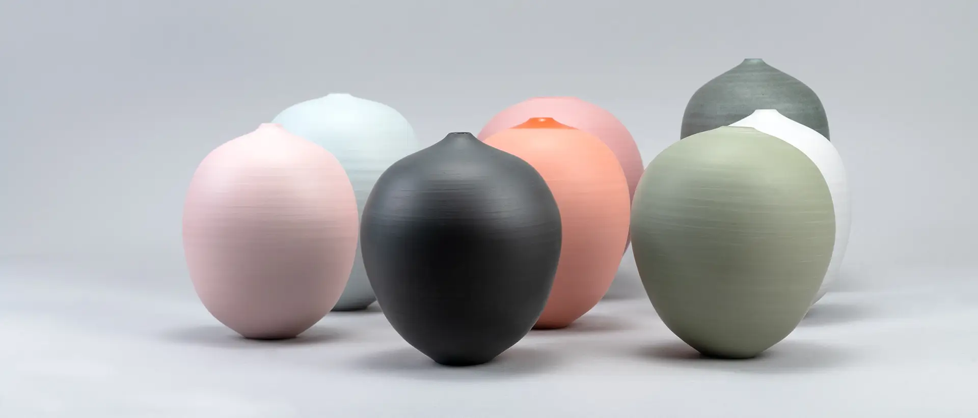 A collection of beautiful hand-thrown ceramic vases sitting together against a plain backdrop