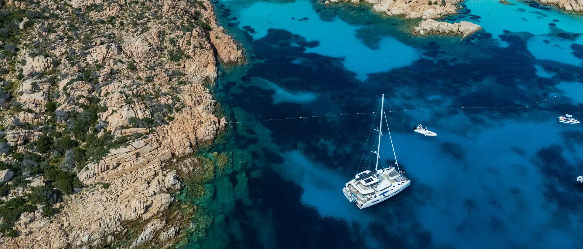 Aerial shot of Arca sailing yacht in blue waters by craggy cliffsides - they are an expert in the your world is calling community