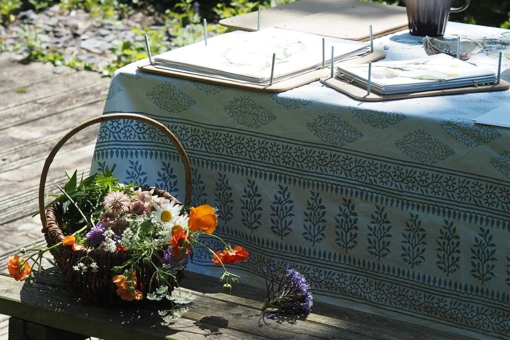 A basket of wildflowers sat on a bench outside by a picnic table with flower presses on it