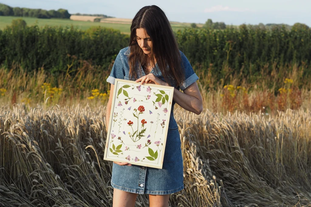 Beth Kendal holding her pressed flower art standing in the Dorset countryside