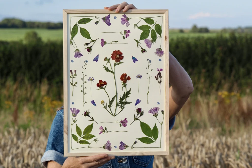 Beth Kendal holding pressed flower art in front of her face in the dorset countryside